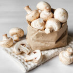 Mushrooms champignons in paper bag on a white wooden table.