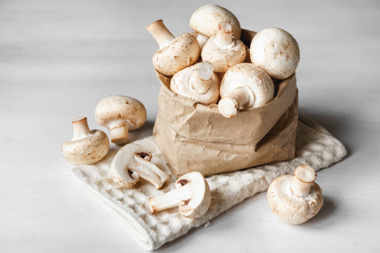 Mushrooms champignons in paper bag on a white wooden table.